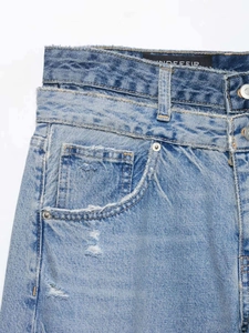 Détail macro d'un jean bleu clair avec double taille et bords effilochés