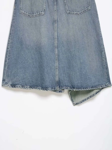 Detail view of the back hem of a blue denim skirt with pockets and contrast stitching