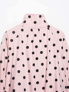 Detail of light pink high neck jacket featuring black polka dots and fine stitching