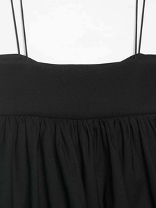 Detail of black camisole showing thin straps and ruffled chest design on woven fabric