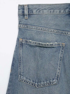 Close-up of light blue denim jeans showing back pocket with distressed edge detail
