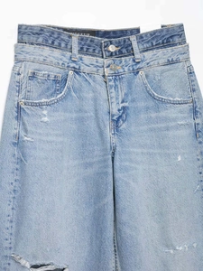 Détail d'un jean bleu clair à taille haute avec double ceinture et finitions délavées usées