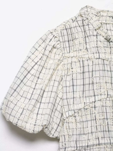 Detail of white plaid fabric with 3D floral embroidery and ruffled collar top