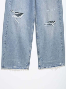Détail d'un jean droit bleu clair avec des trous aux genoux et des ourlets effilochés