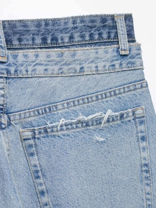 Détail du jean bleu clair avec double ceinture superposée et poches usées au design chic