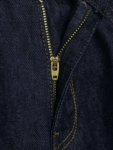 Close-up of high-quality YKK metal zipper and orange stitching on dark blue denim fabric
