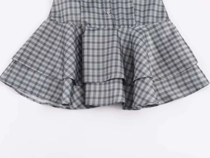 Detail of grey gingham plaid dress featuring layered ruffle hem and small white button