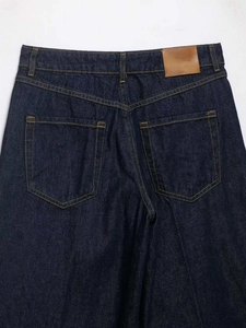 Detail view of dark blue denim jeans with contrast stitching and blank leather waist patch
