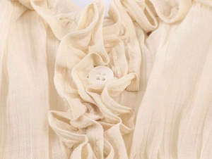 Detail of cream pleated fabric with ruffle edges and a small white round button