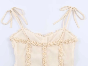 Detail of cream lace camisole featuring delicate shoulder bows and vertical ruffle trim