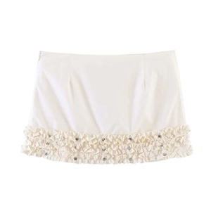 Detail of ruffled beige mini skirt featuring tiered hem and decorative metal studs