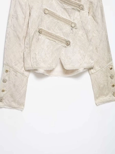 Macro detail of cream jacquard fabric texture and decorative metal buttons on a military jacket
