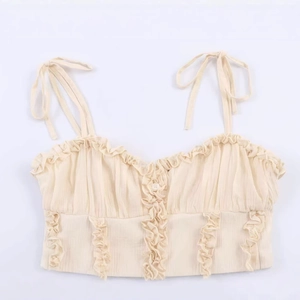 Beige crop top featuring tie-up straps with ruffled edges and front buttons
