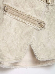 Close-up of beige jacquard jacket featuring vintage metal buttons and frayed edges
