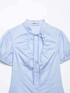 Detailed view of light blue poplin shirt with pleated collar and bow tie neckline