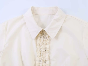 Close-up of white summer shirt featuring zipper closure and ruffled trim with metal studs