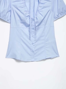 Detail of light blue poplin shirt featuring ruffled collar and bow tie closure