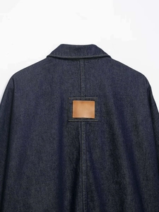 Detail of dark blue denim jacket back featuring a square brown leather patch and stitching