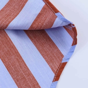 Detail view of brick red and light blue striped cotton fabric with white stitching