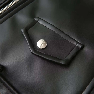 Détail d'une veste en cuir noir avec poche à bouton argenté et textures de fermeture éclair