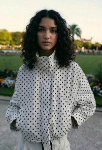 Détail d'une veste blanche à pois avec col montant et fermeture éclair à cordon