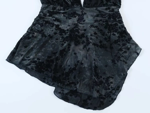 Dettaglio di pizzo nero semitrasparente con floccaggio floreale e taglio asimmetrico