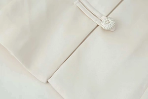 Detail of elegant cream jacket showing handmade frog button closures and textured fabric