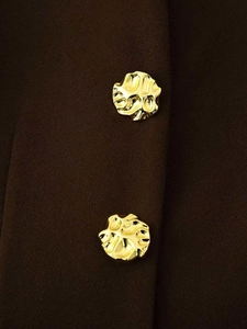 Macro detail of dark brown wool coat featuring unique textured gold metallic buttons
