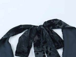 Dettaglio del tessuto mesh nero burnout a fiori annodato in un fiocco sul colletto