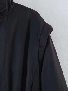Detail der schwarzen Stehkragenjacke mit strukturierter, überlappender Schulterpartie