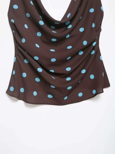 Detail view of brown sleeveless top featuring blue polka dots and a draped cowl neckline