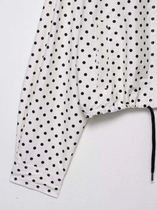 Détail du tissu à pois blancs avec ourlet à cordon noir et poignets à boutons élégants