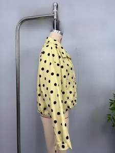 Close-up of lightweight pale yellow jacket featuring large black polka dots and buttons