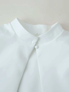 Close-up of a white high-neck shirt with a central bead button and size label S detail
