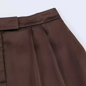 Detailed close-up of dark brown satin high waist shorts with elegant pleated textures