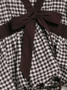 Detail of gingham patterned top featuring a dark brown bow tie and ruffled fabric texture