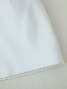 Close-up of the white woven fabric texture and hem stitching on women's cape style top