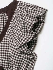 Detail of gingham patterned top showing ruffled sleeves and elastic brown cuffs