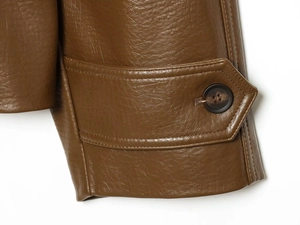 Détail de la manche d'une veste en simili cuir marron foncé avec bouton et coutures précises