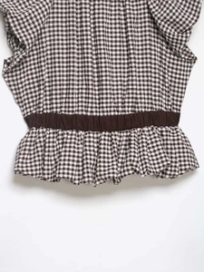 Close-up of brown gingham top featuring elastic smocked waist and ruffled hem details