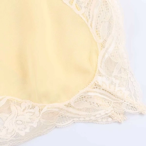 Close-up of delicate beige lace trim on pale yellow satin fabric camisole top