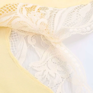 Detailed close-up of delicate white floral lace trim on soft yellow satin fabric