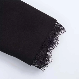 Detail of black woven fabric with intricate eyelash lace trim on the sleeve and hem