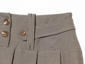 Detail of high-waisted pleated skirt featuring brown houndstooth pattern and double buttons