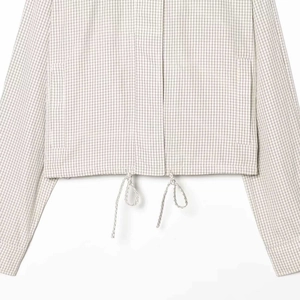 Détail de la veste à carreaux avec cordon de serrage réglable et poches latérales