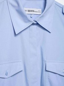 Détail du col d'une chemise bleu clair avec poches poitrine et étiquette de marque