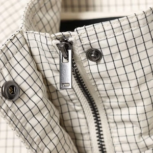 Détail d'une veste à carreaux avec fermeture éclair métallique et boutons pression