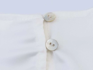 Detailed macro shot of elegant double pearl button closure on a white chiffon blouse