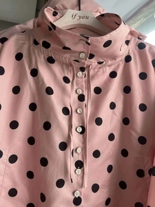 Close-up of pink polka dot blouse with high collar and white buttons on a wooden hanger