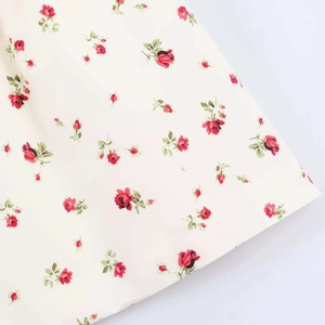 Gros plan détaillé du tissu floral avec roses rouges et feuilles vertes sur fond crème